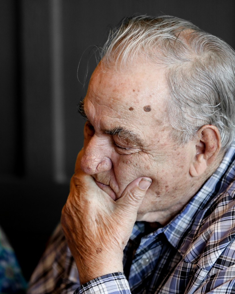 An elderly man deep in thought, resting his hand on his chin, wearing a plaid shirt, symbolizing contemplation and the challenges of aging.