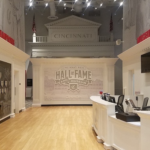 Cincinnati Reds Hall of Fame and Museum entrance with white counter, wooden floor, and wall art depicting historical elements.