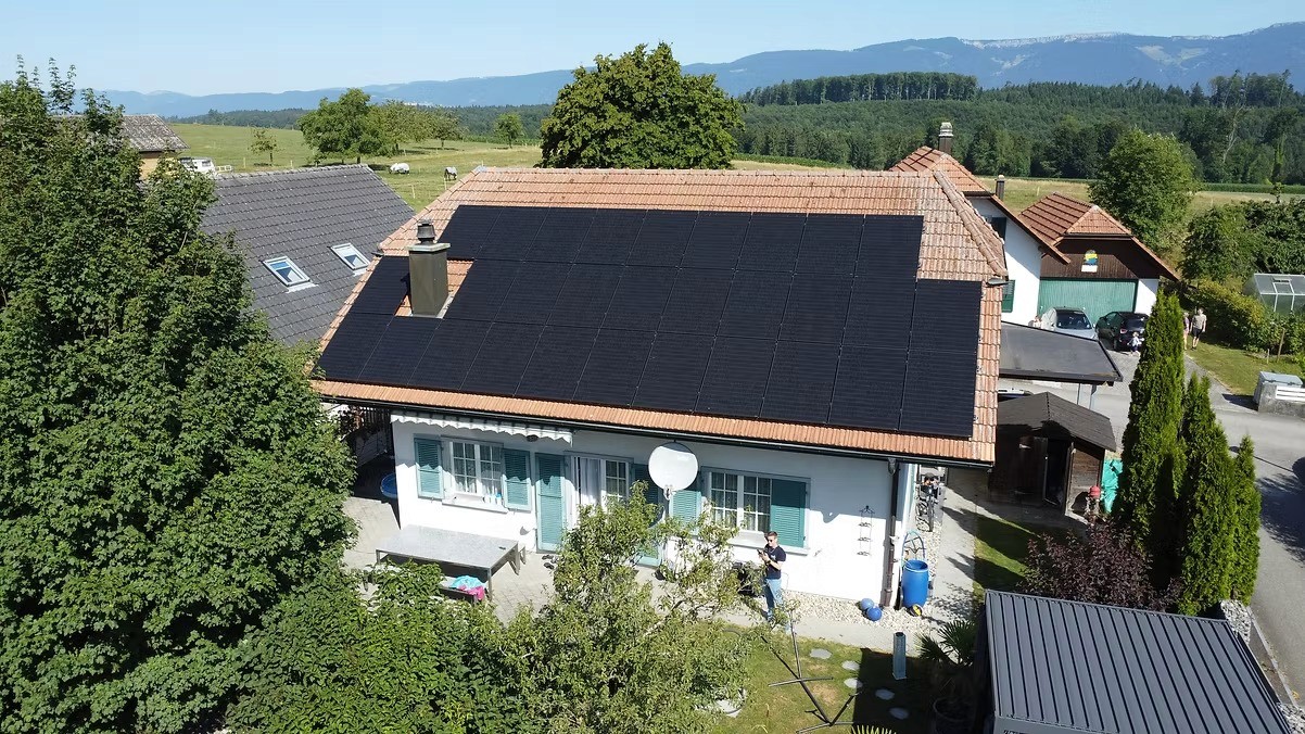 Bäume im Vordergrund vor einem Haus mit Solaranlage.