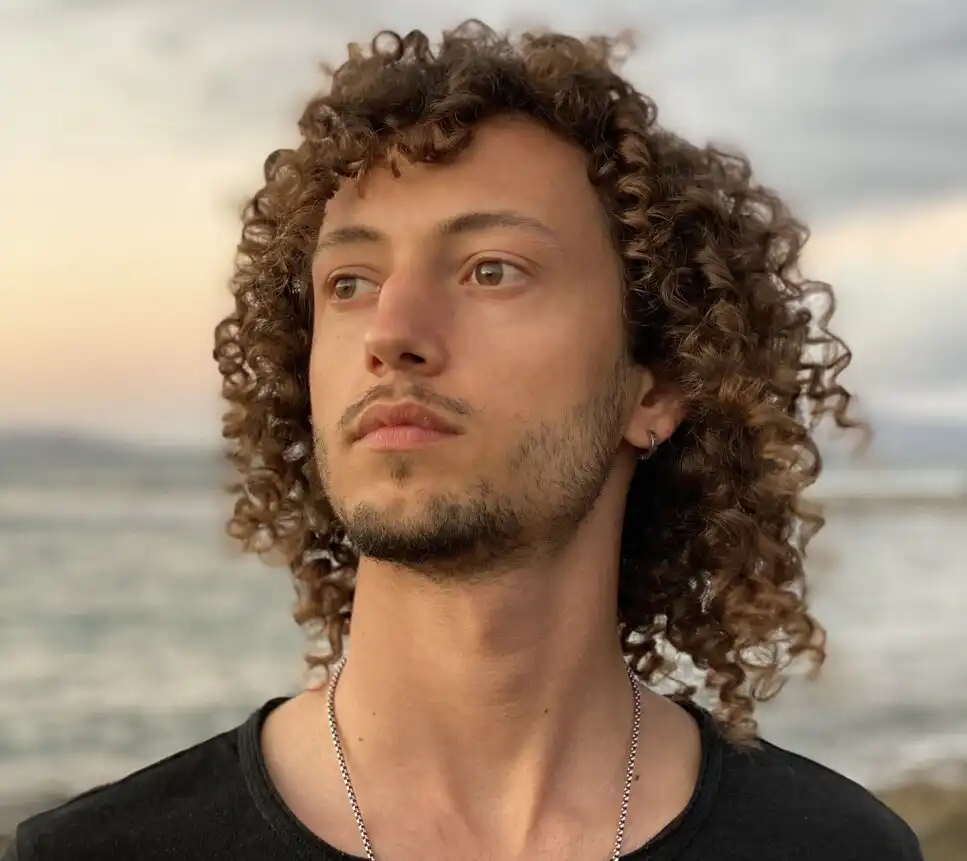 Thiago Calderaro, Founder and CEO of CoachingArea, with curly hair and wearing a black shirt, gazing thoughtfully towards the horizon with a calm ocean in the background. He is the author of this article.