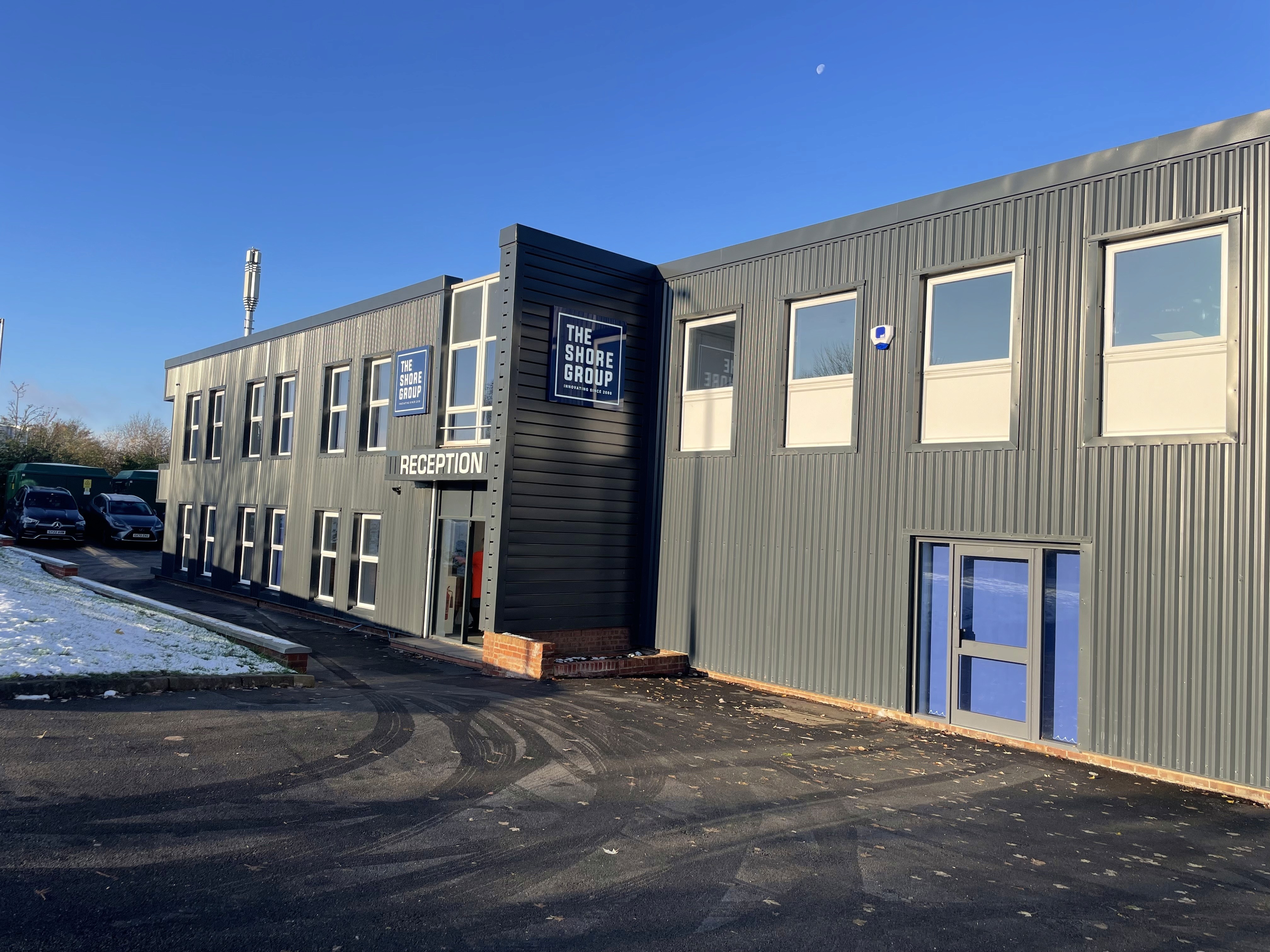 A group of construction workers wearing high-visibility jackets and hard hats celebrate at a construction site with safety signs and equipment visible in the background.