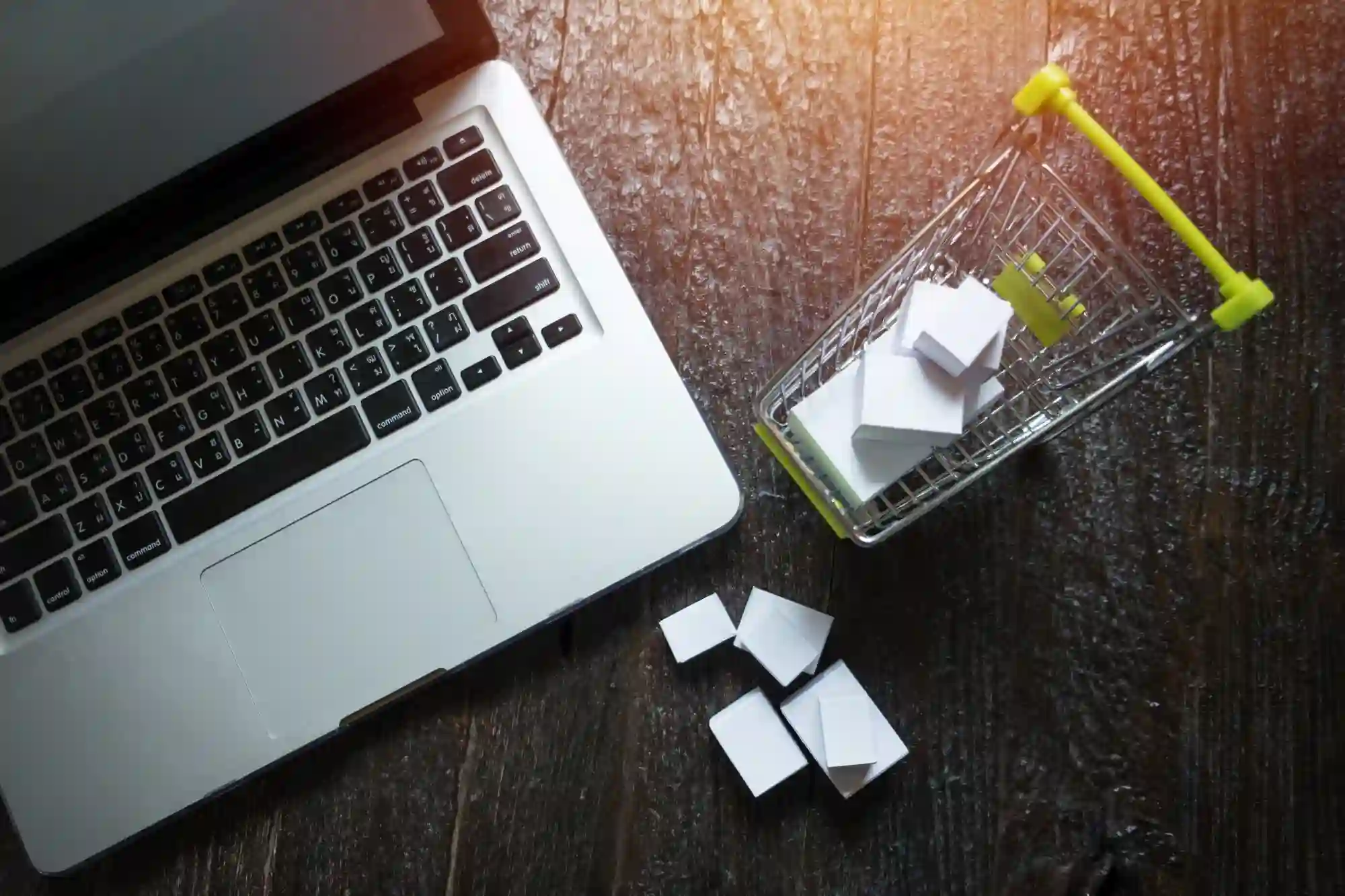 Miniature shopping cart with boxes next to a laptop, representing online ordering and e-commerce logistics.