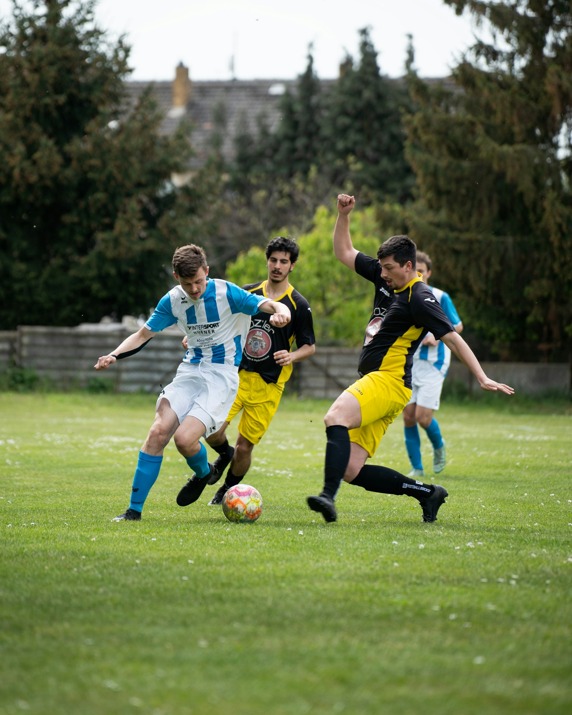 A soccer player in a blue and white striped jersey dribbling the ball while being challenged by a defender in black and yellow.