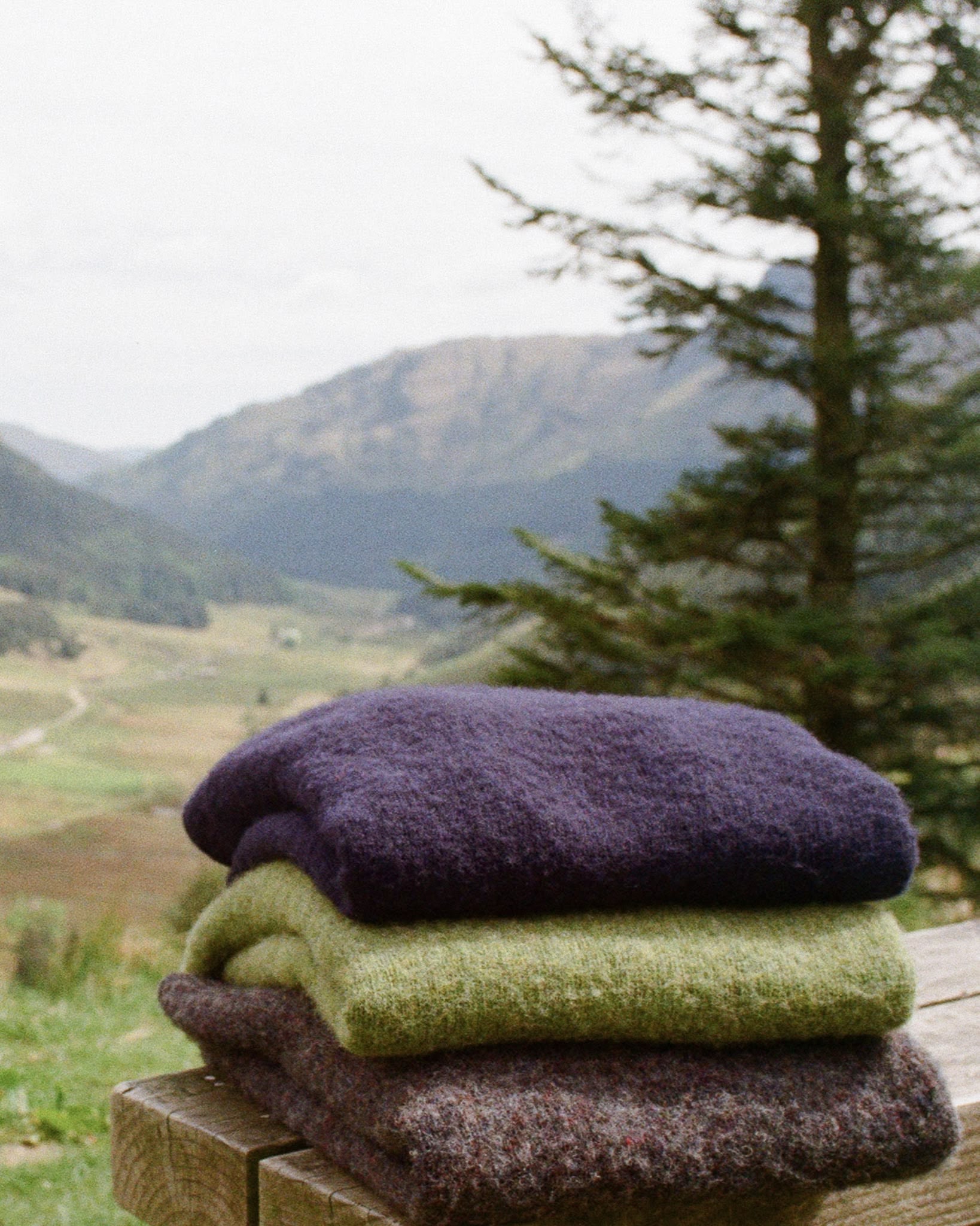 Nature morte de pulls pliés marine, vert et marron sur un banc dans la campagne Ecossaise