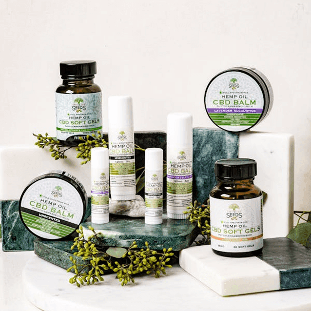 Group of CBD wellness products including balm, soft gels, and topical sprays displayed with greenery on a marble surface