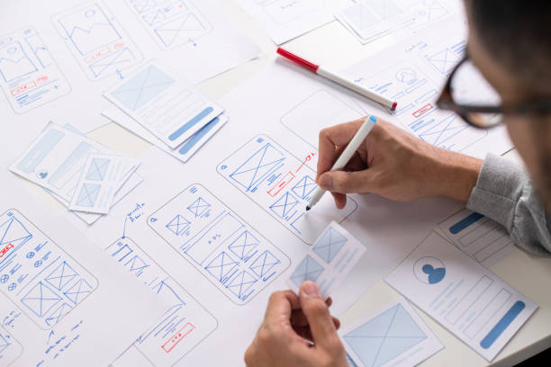 UI/UX designer sketching app wireframes on paper with pen. Mobile app design process.