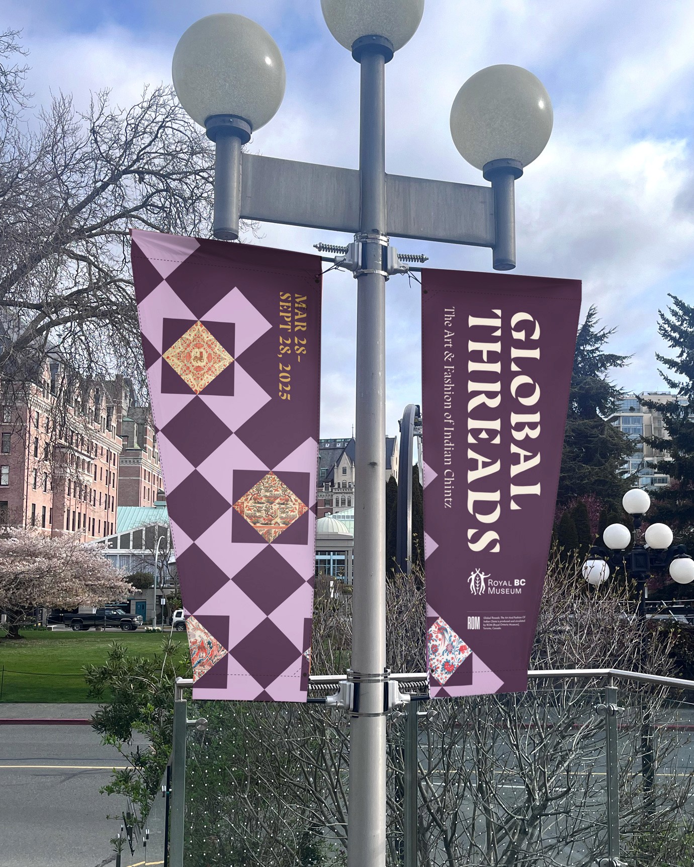 A set of two vertical lamppost banners for an exhibition titled Global Threads