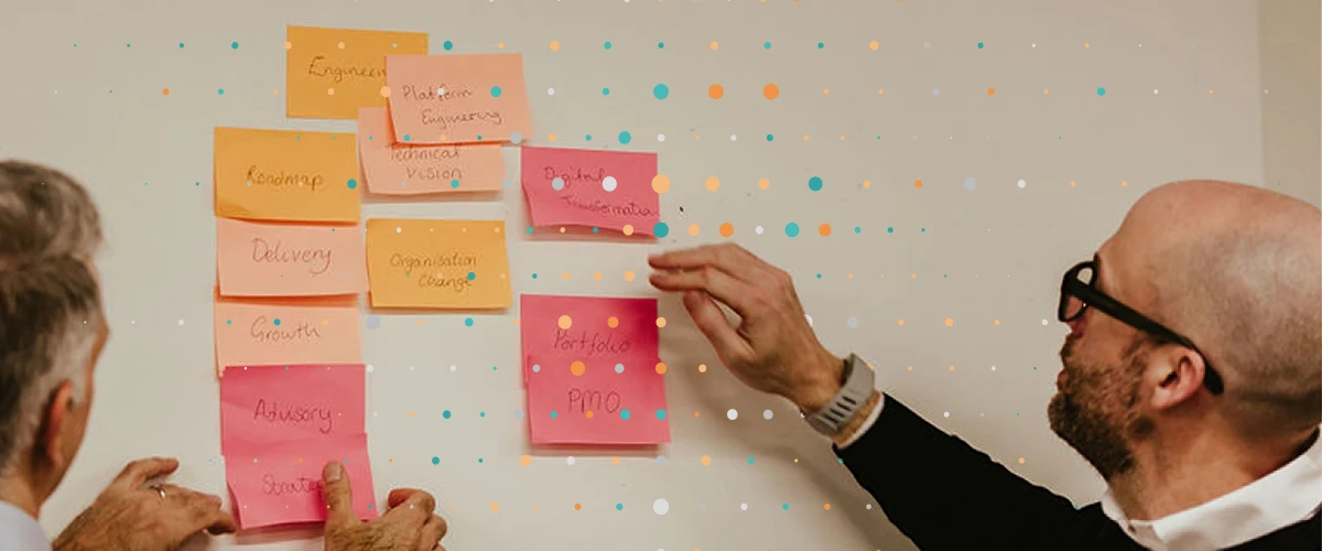 two consultants reviewing a list of post it notes on a wall