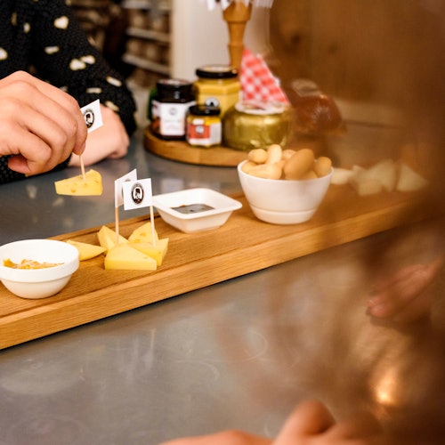 手正在挑选放在木制托盘上的奶酪块、小碗和各种食物，它们展示在厨房台面上。