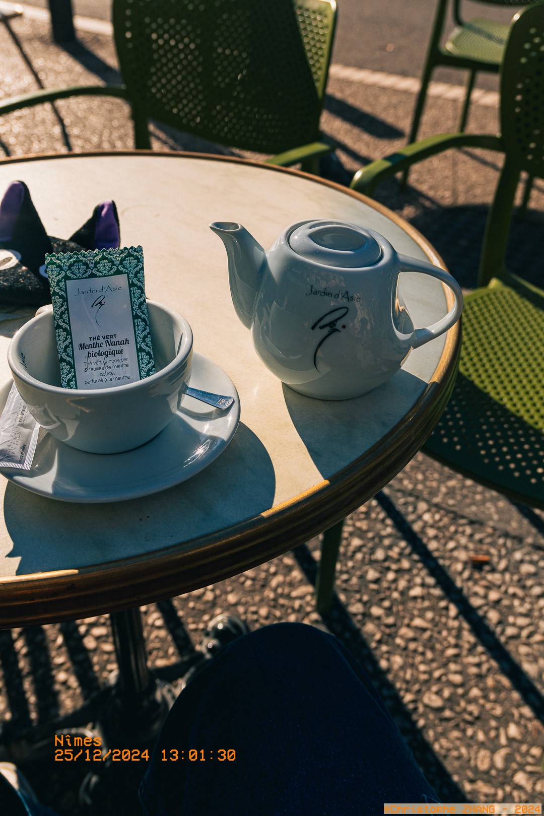 Théière blanche et tasse avec un sachet de thé à la menthe, sur une terrasse ensoleillée à Nîmes.