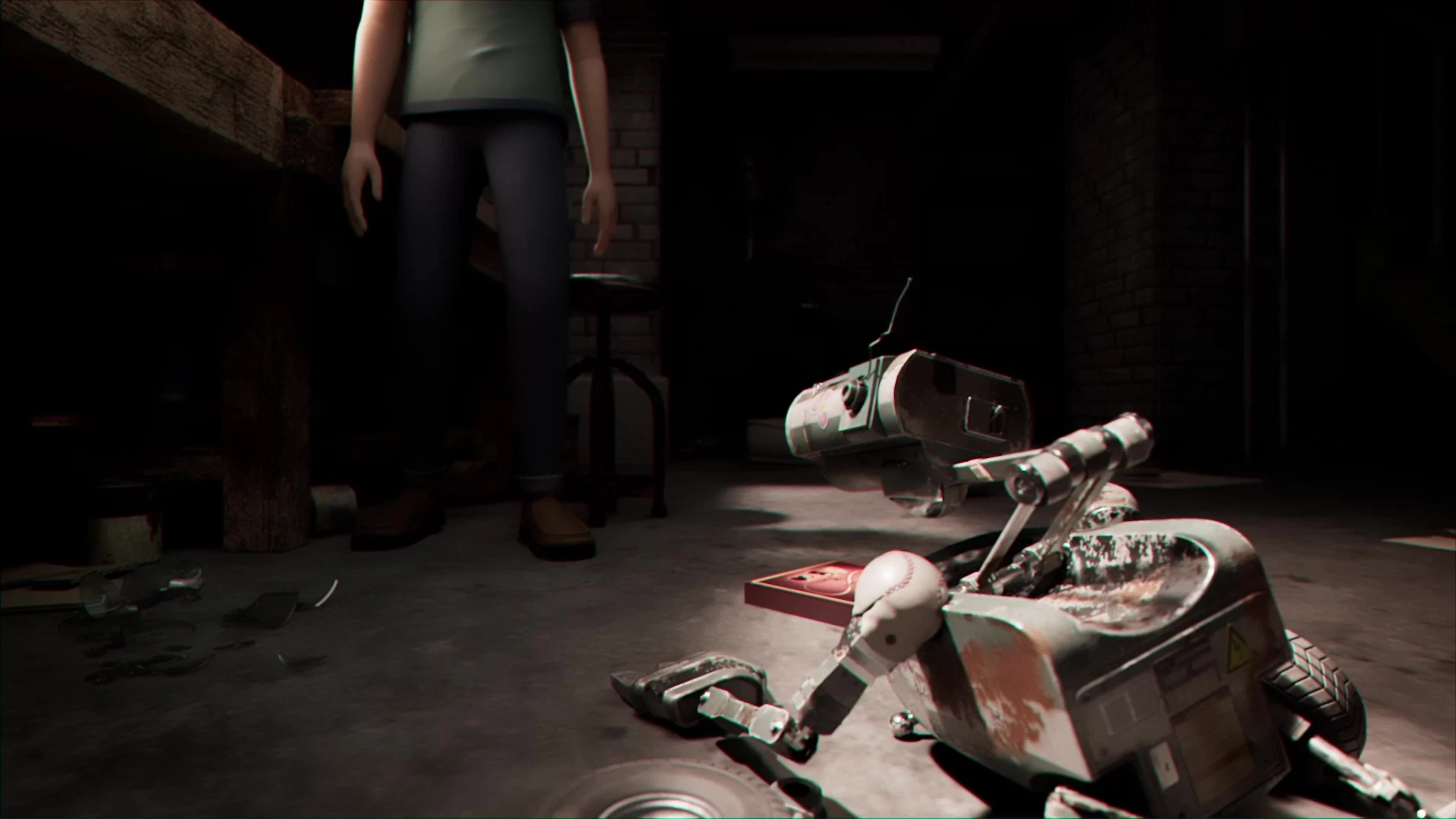 A robot with a broken leg, lies on the ground as a man stands in the background