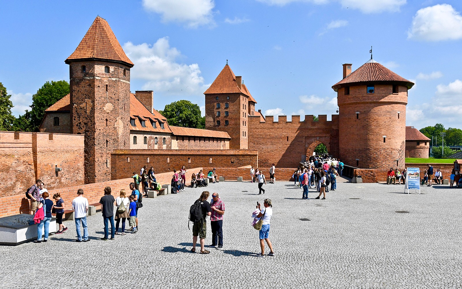 Odwiedzający zwiedzający dziedziniec zamku Malbork z przewodnikami audio.