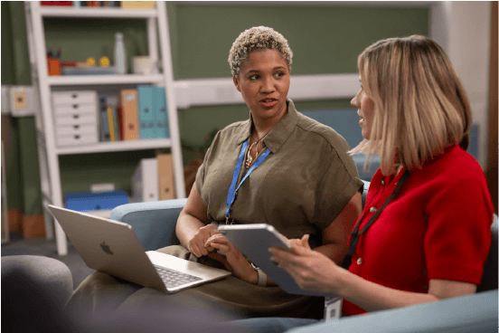 Zwei Lehrerinnen besprechen Inhalte auf einem MacBook in einer Schulbibliothek