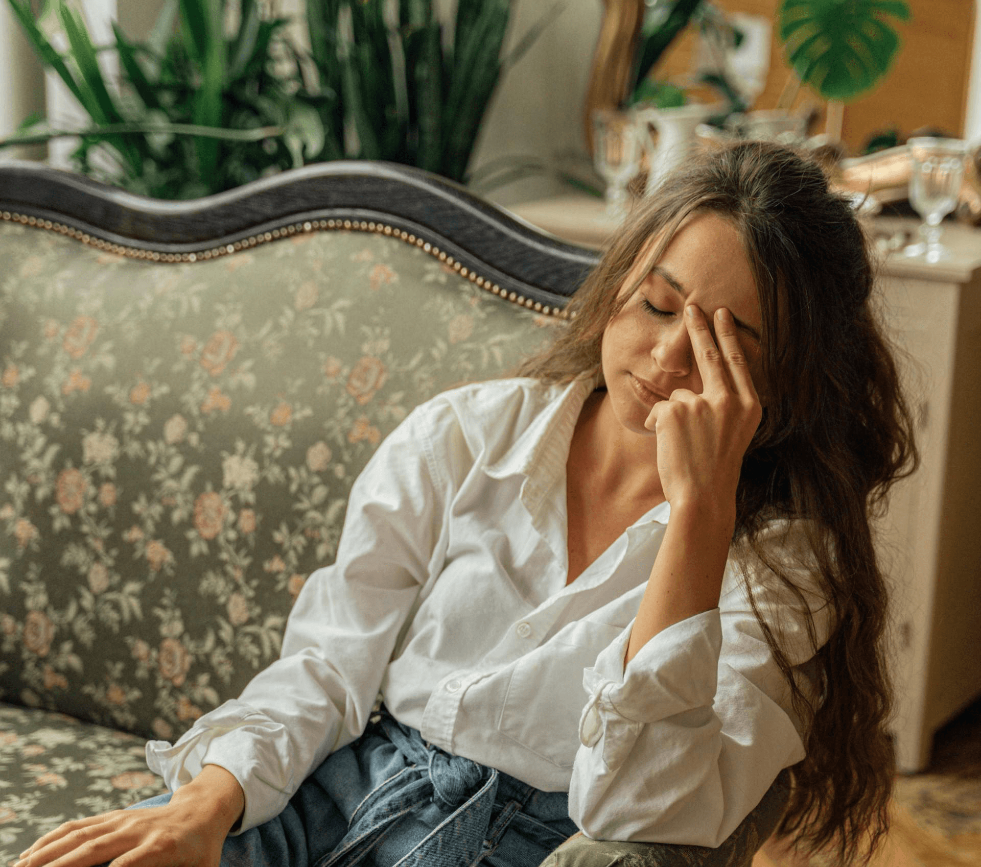 Woman sitting on couch with hand on forehead, feeling stressed and anxious