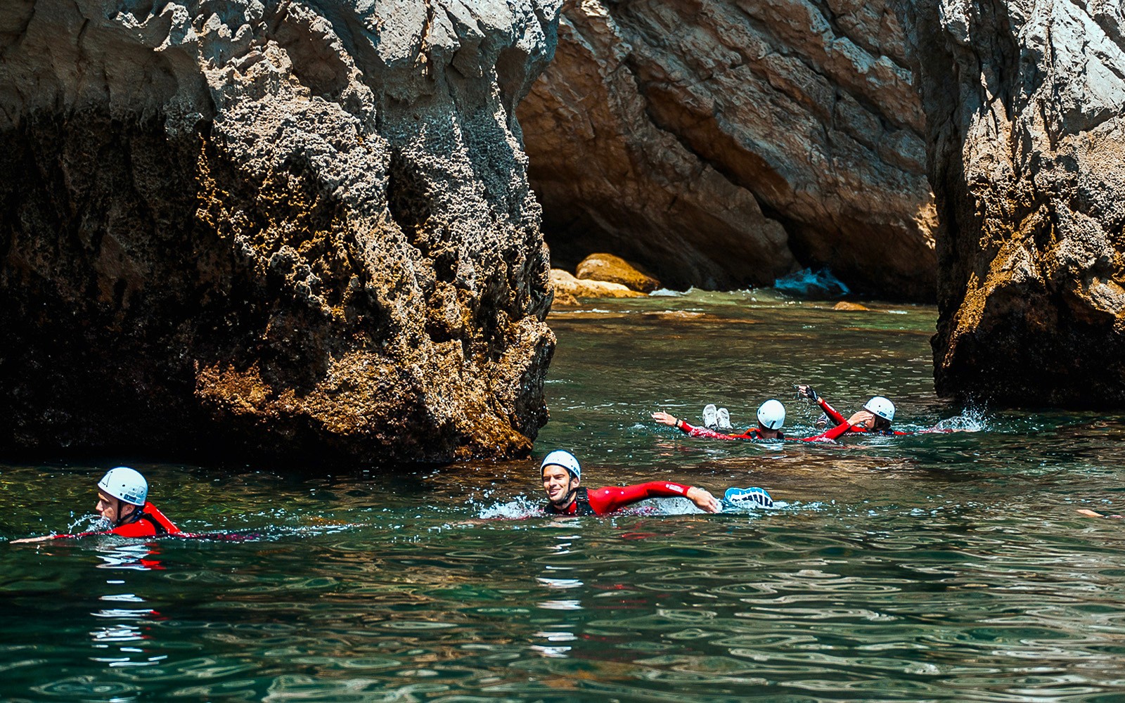 Eventyrere som driver med kystvandring nær de steinete klippene i havet, iført hjelmer og våtdrakter.