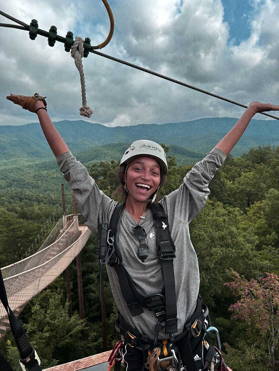 A girl in zipline harness waving her arms above the treetops of the Smoky Mountains