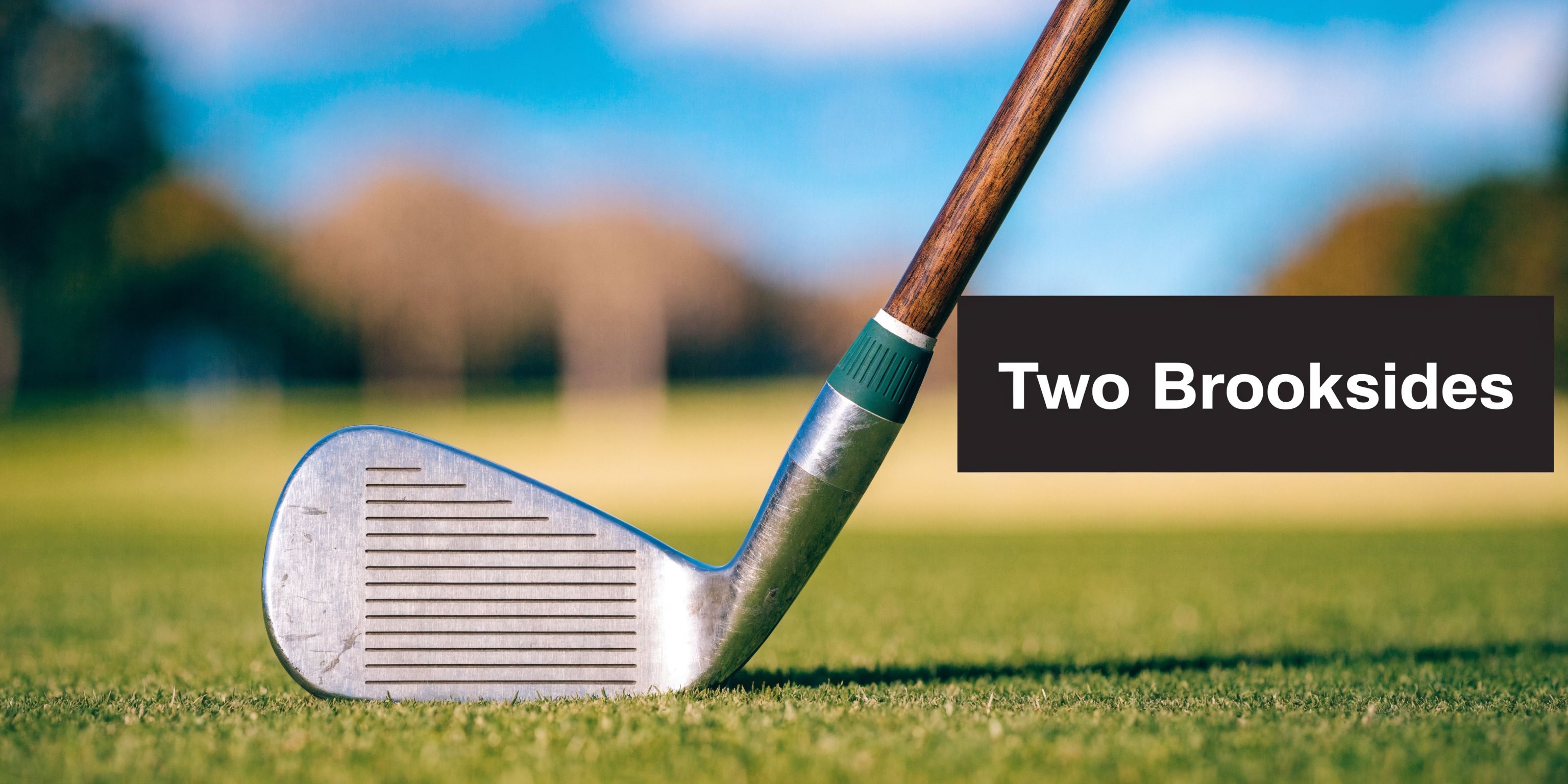A classic metal golf iron resting on a lush green grass golf course during a sunny day.