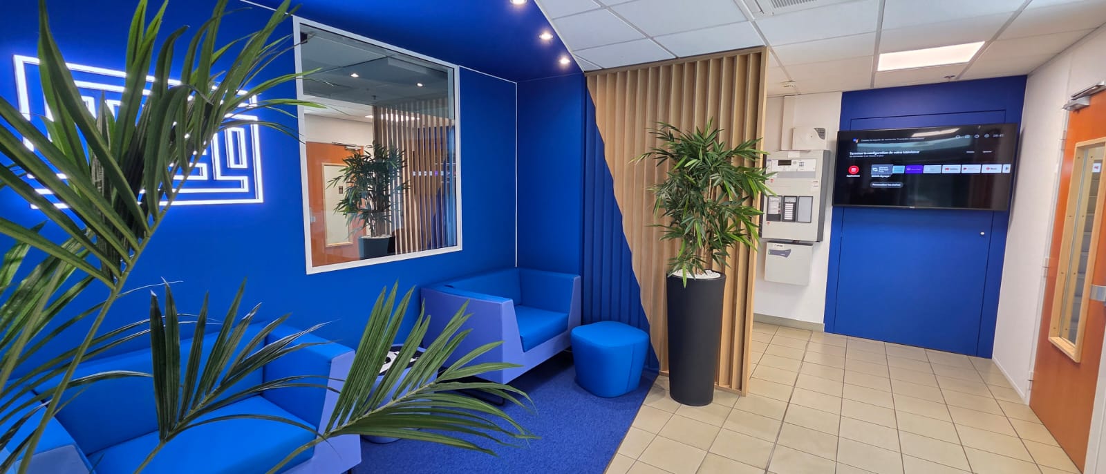 Showroom WEG – Espace d'accueil sur-mesure bleu avec logo mural rétroéclairé, mobilier lounge et écran digital intégré, conçu et réalisé par Expace
