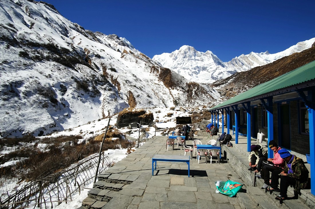 Trekkers resting outside a teahouse beneath snow peaks