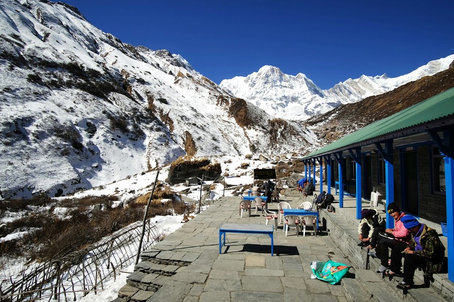 Trekkers resting outside a teahouse beneath snow peaks