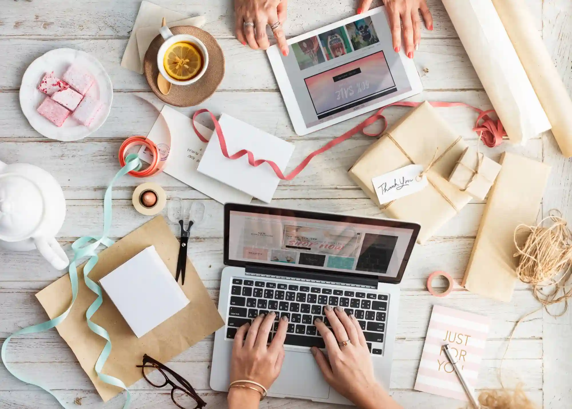 Overhead view of two people working on a laptop and tablet, surrounded by gift wrapping supplies.