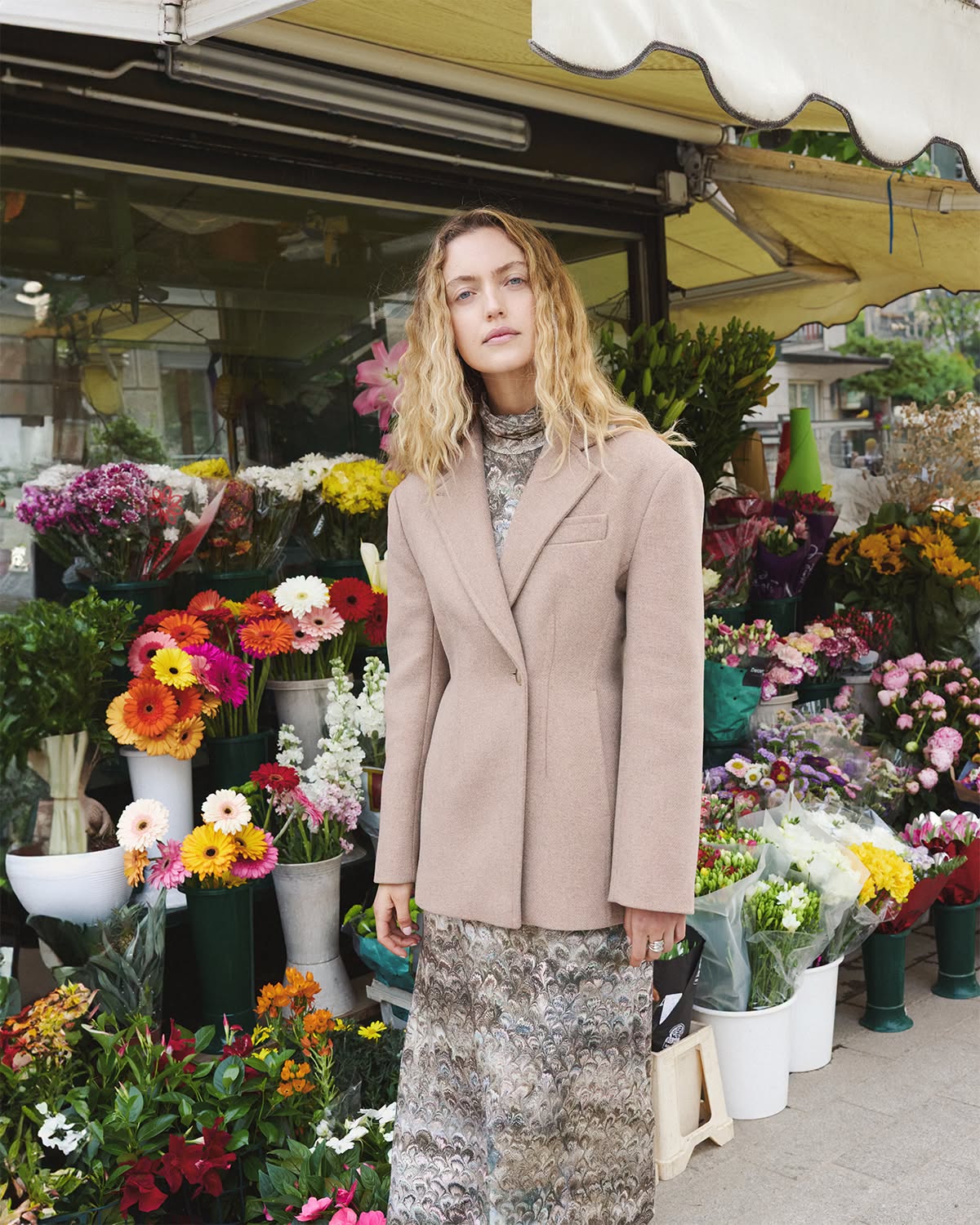 Donna con blazer beige davanti a un banco di fiori