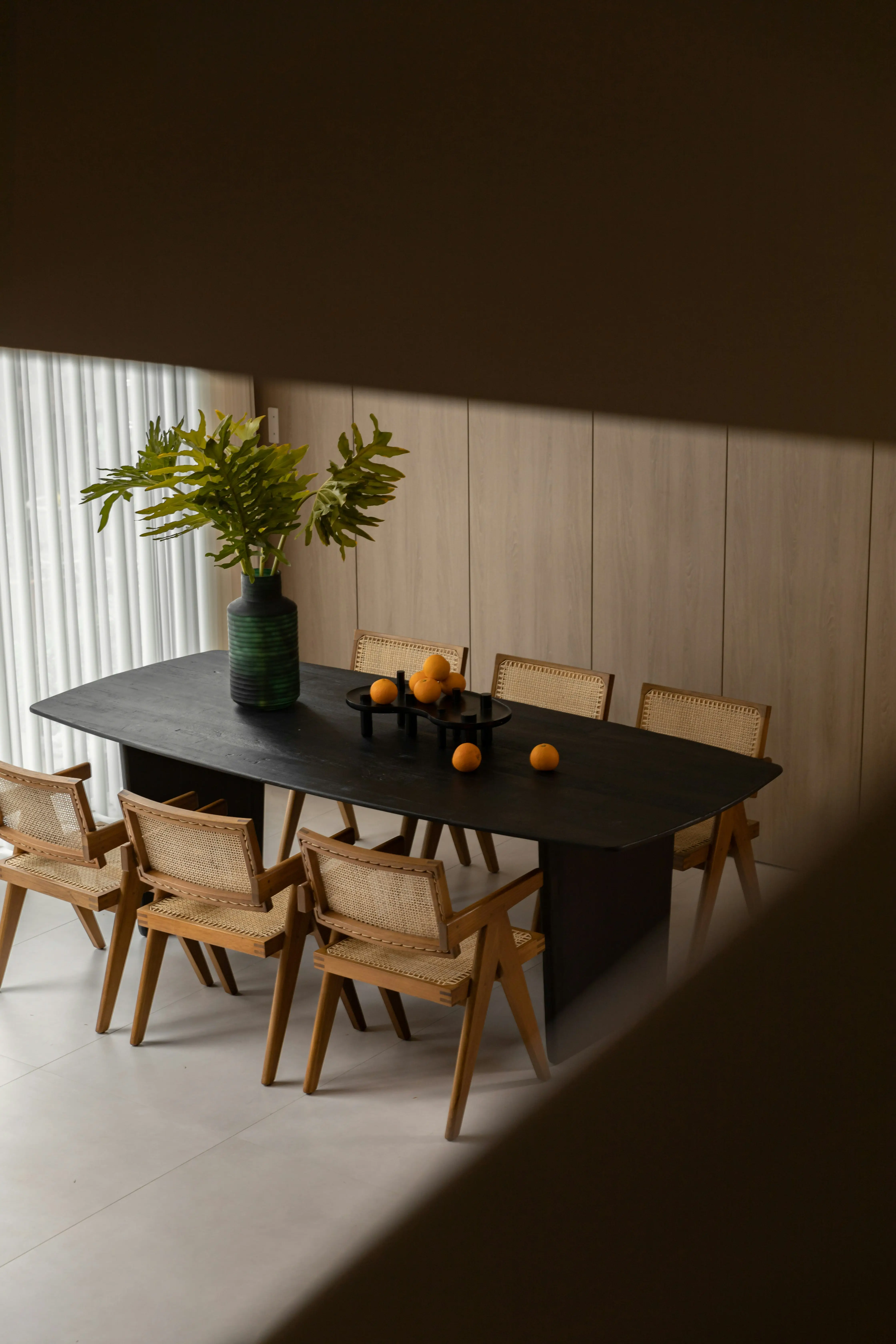 A dining table set with chairs, vase, and fruit. 