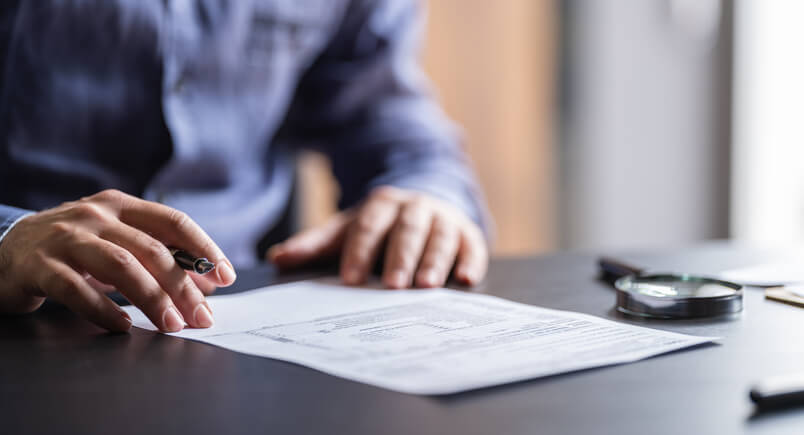 A man is signing a document on a wooden table, focused on the task at hand. Form G-28