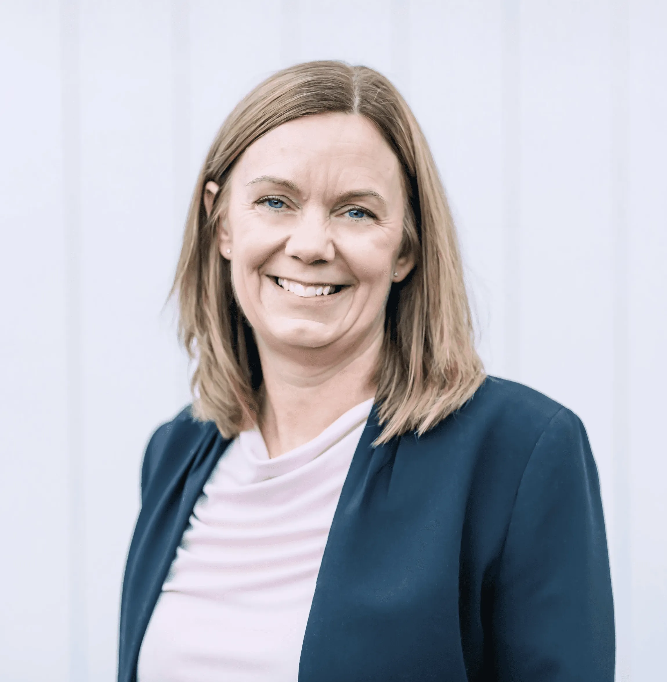 Maria Johansson ler, klädd i kavaj, mot en vit bakgrund.