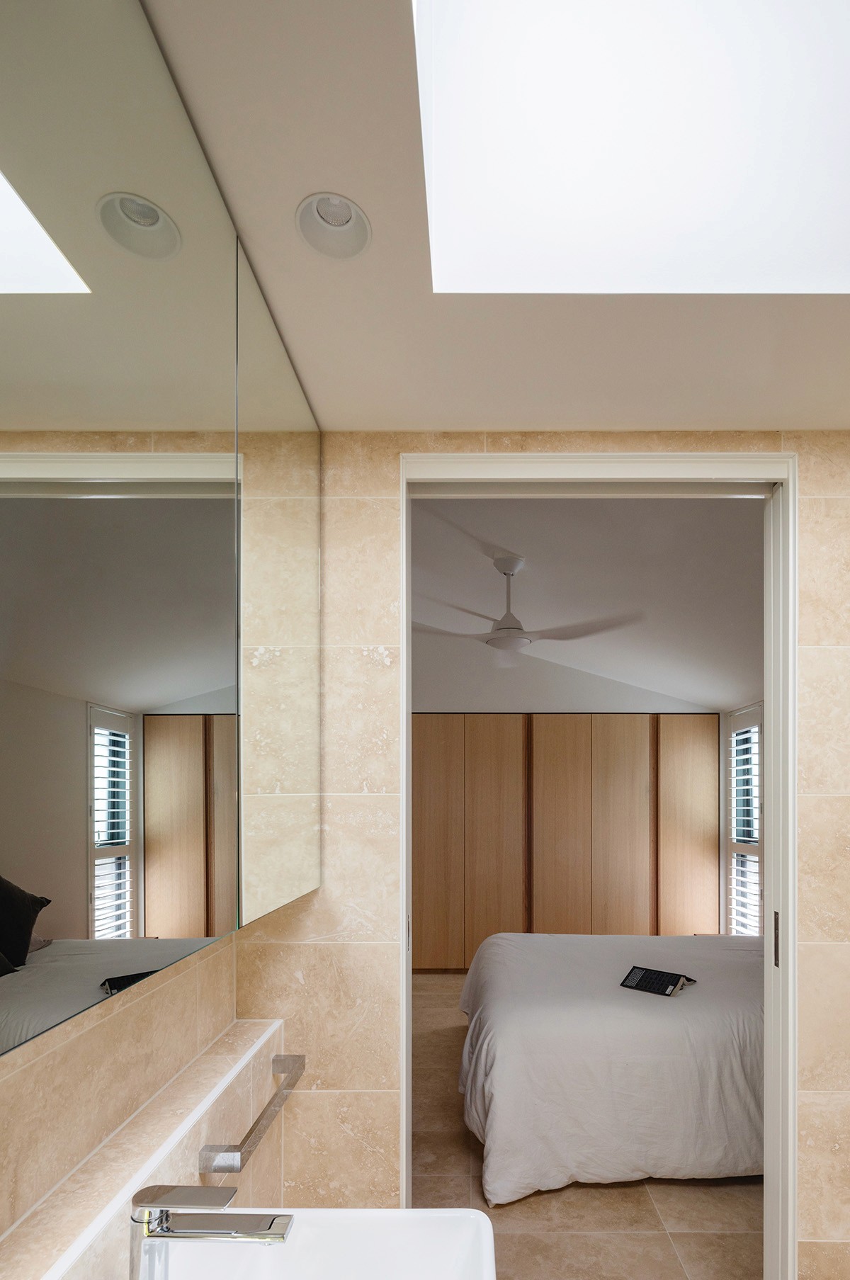 Ensuite bathroom with travertine surfaces, integrated basin, and a framed view back toward the bedroom, reinforcing the home’s compact and cohesive design.