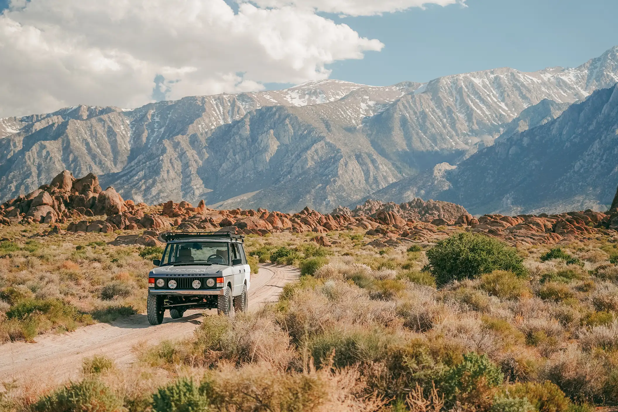 A silver Range Rover SUV parked on a dirt road with mountains in the distance.