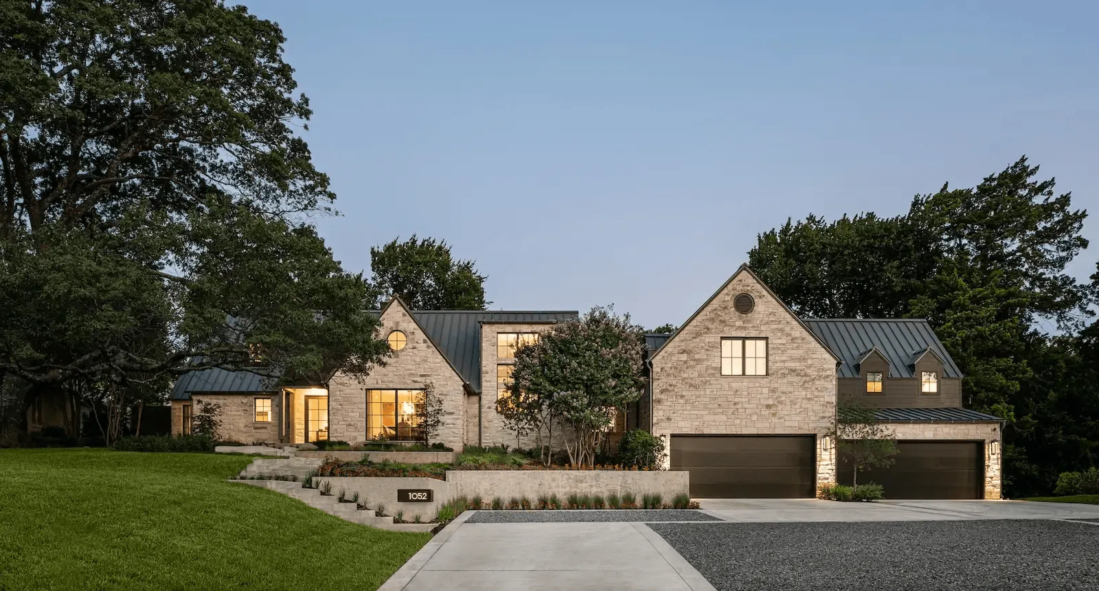 Modern two-story house with stone facade, metal roof, and dual garage doors.