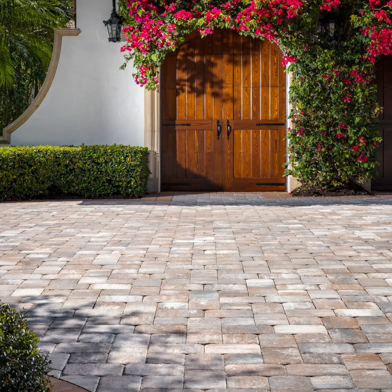 Warm interlocking paver courtyard leading toward a wooden gate framed by flowering plants.
