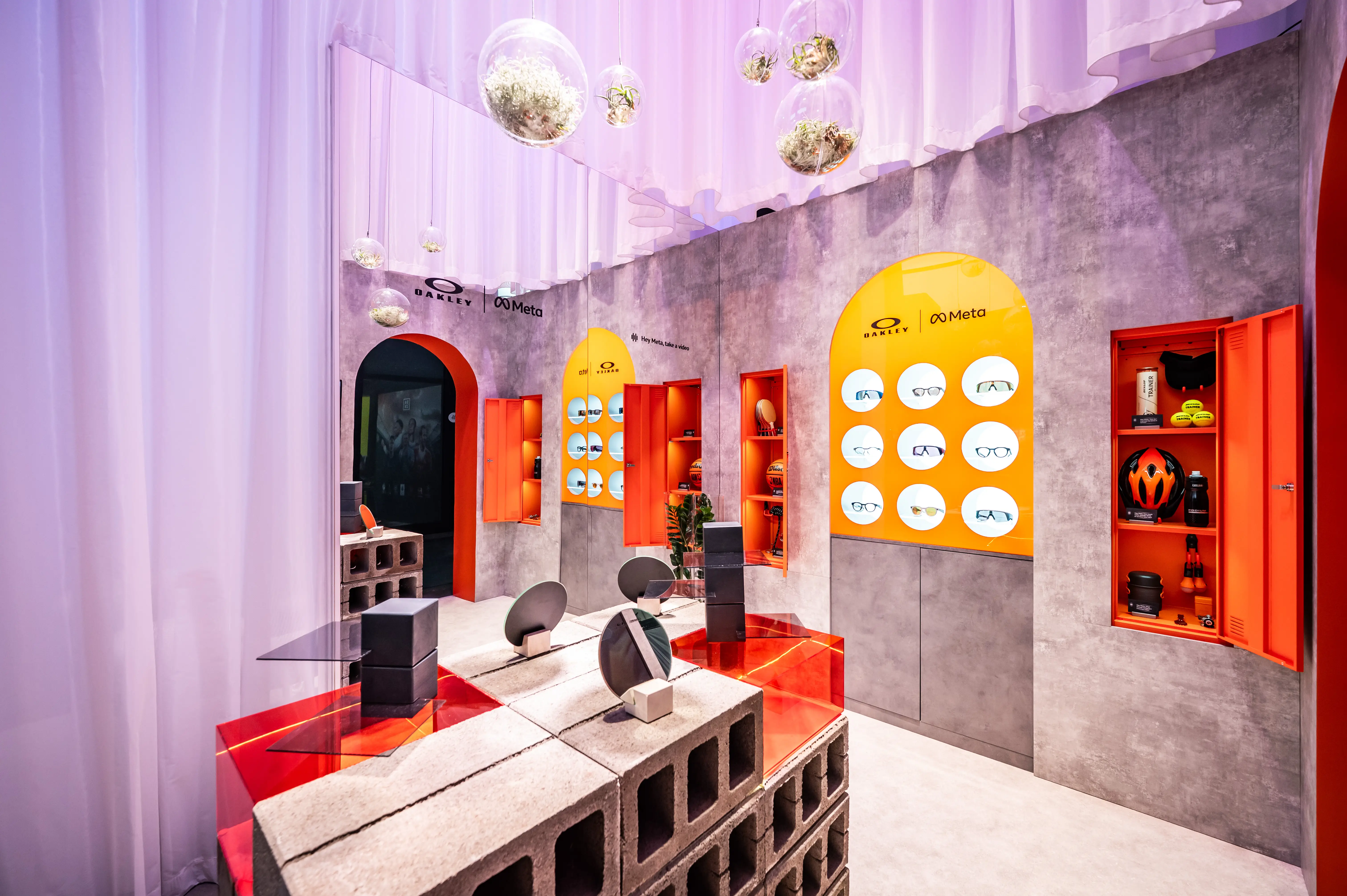 Oakley Meta product walls with glasses displays in orange niches and red acrylic tables on brick plinths.
