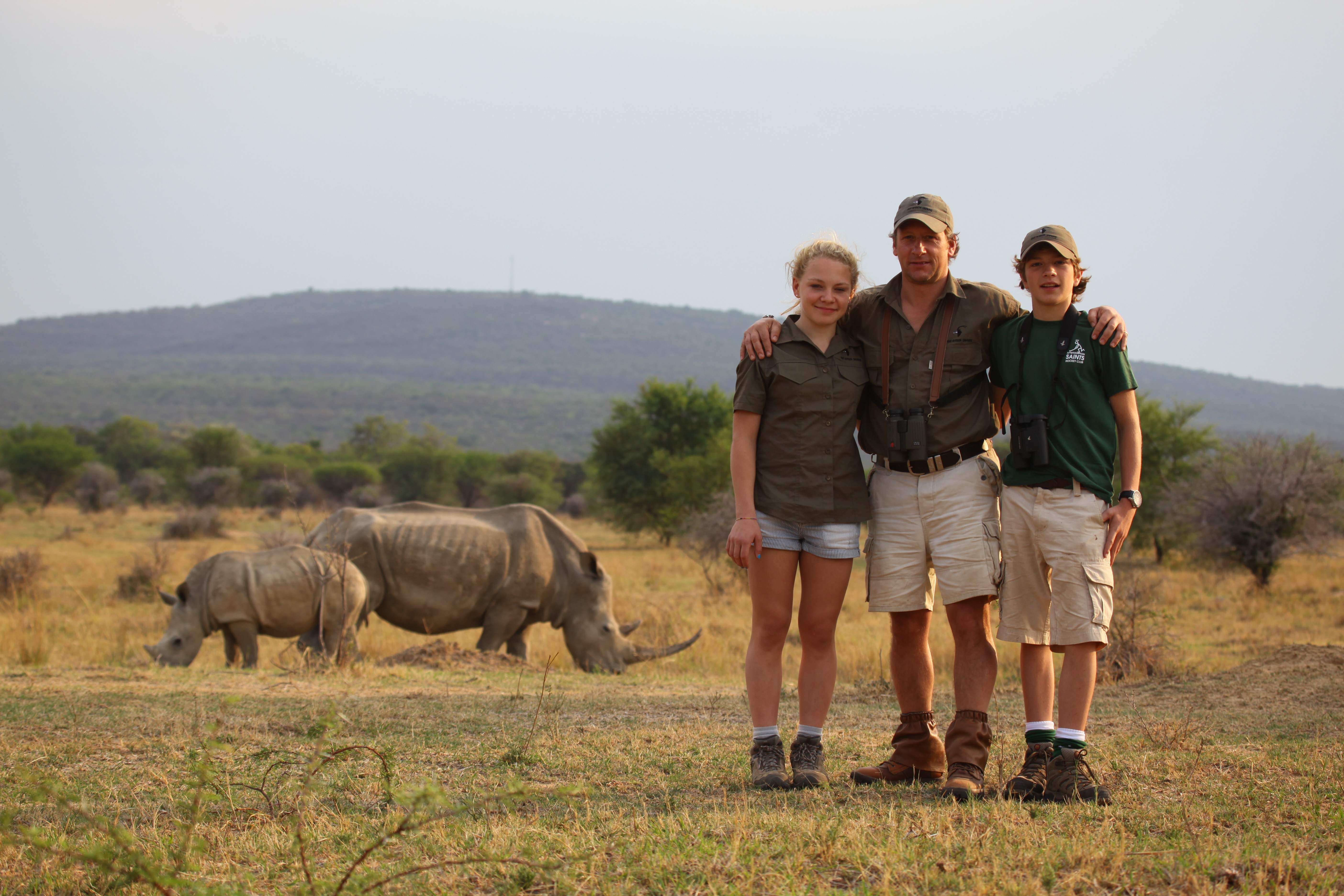 Grupp av ryttare på ridresa i Afrika galopperar över Serengetis vidsträckta slätter medan damm och gnuhjordar rör sig över horisonten under the great migration.