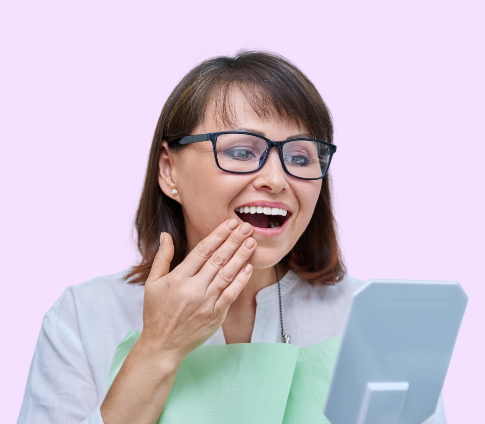 Kvinne ser fornøyd på smilet sitt i speilet etter tannbehandling.