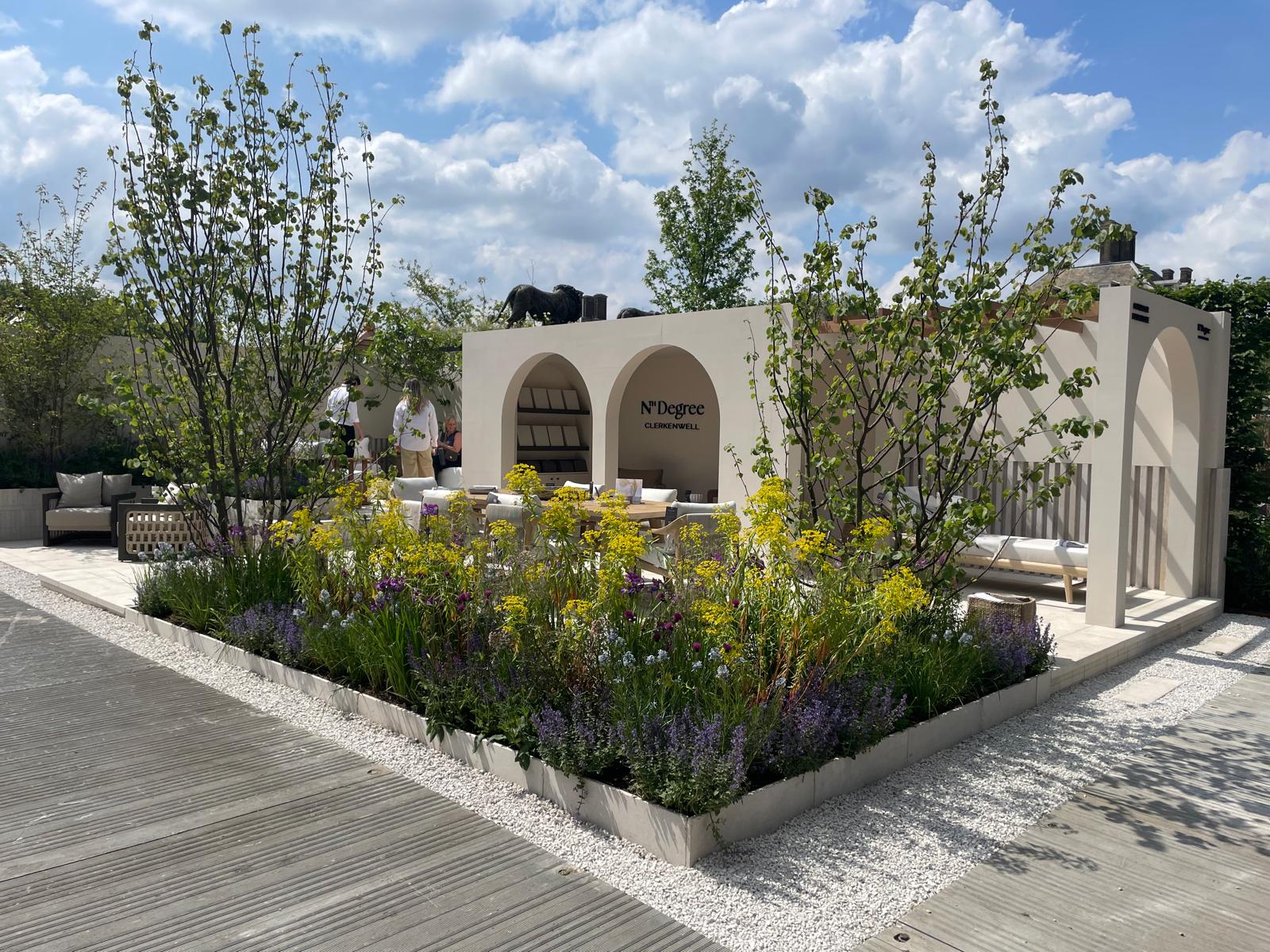 A landscaped area featuring a stone structure with arches, surrounded by greenery and blue skies.