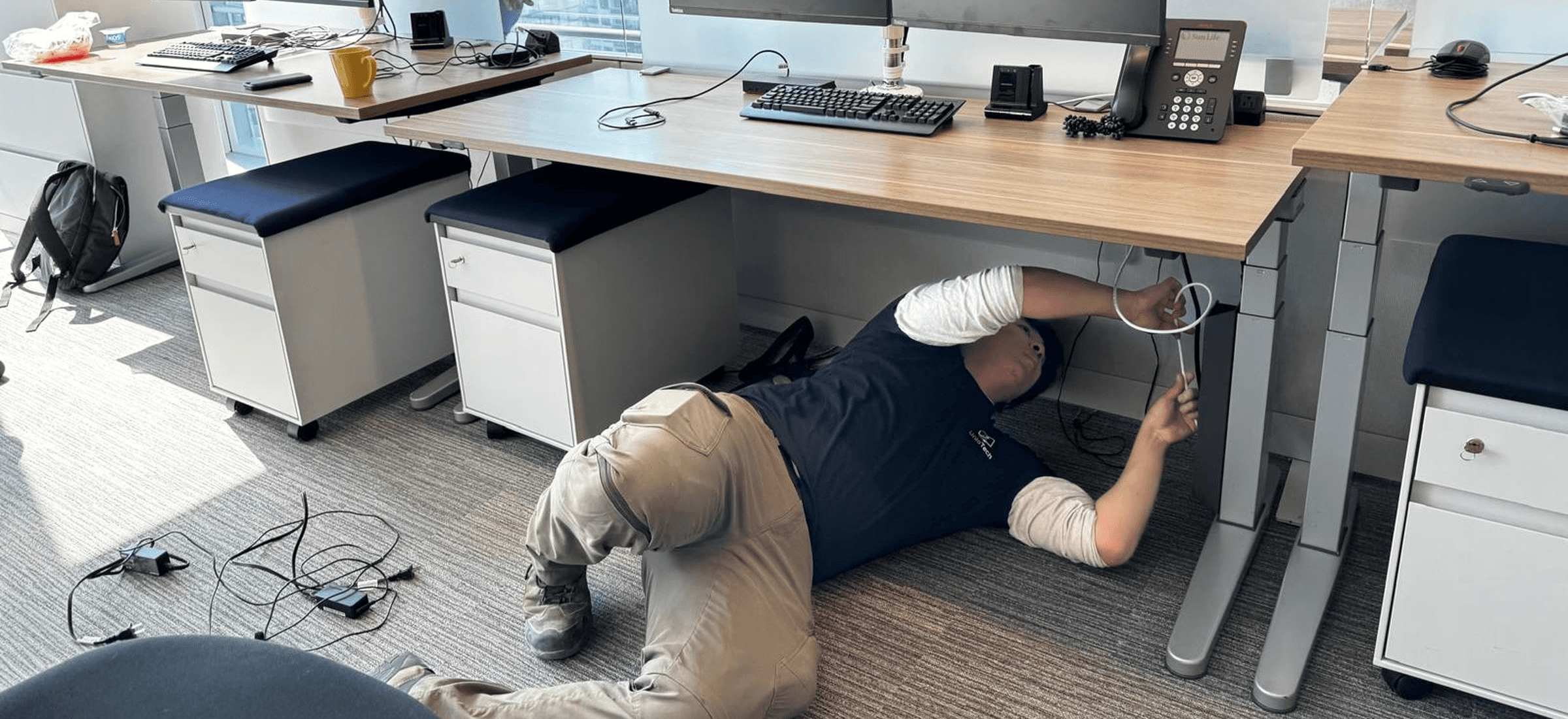 Unio Tech technician managing cables under a workstation during an office relocation