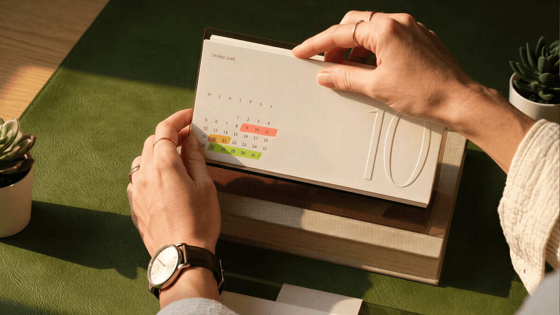Calendário de mesa aberto na página de outubro, com dias marcados em cores para organização de prazos e compromissos.