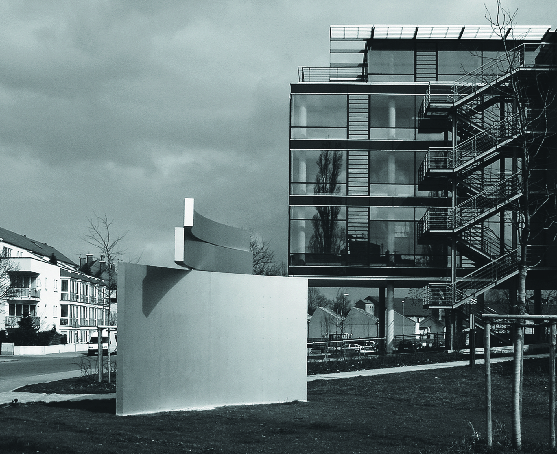 Schwarzweißfoto der Bandskulptur auf einem Sockel vor einem Bürogebäude mit Außentreppe