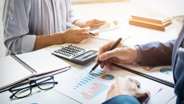 Two business people analyzing charts, using calculator and tablet.
