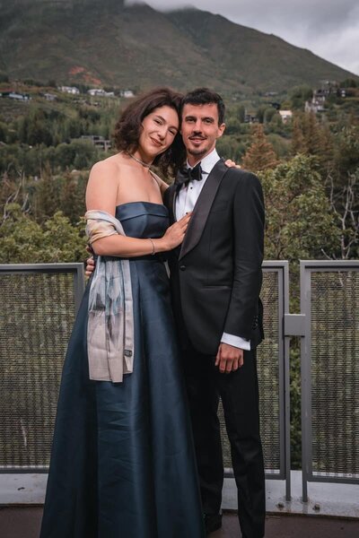 Couple in a blue gown and black tuxedo embracing on a terrace overlooking the mountains