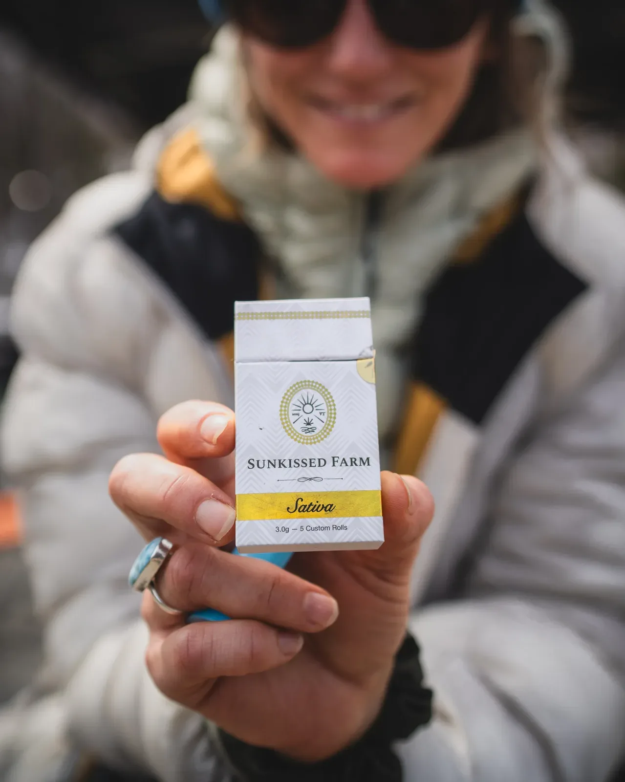 Woman holding a Sunkissed Farm sativa pre-roll pack outdoors in Vermont, where cannabis can be legally consumed in private residences and designated spaces