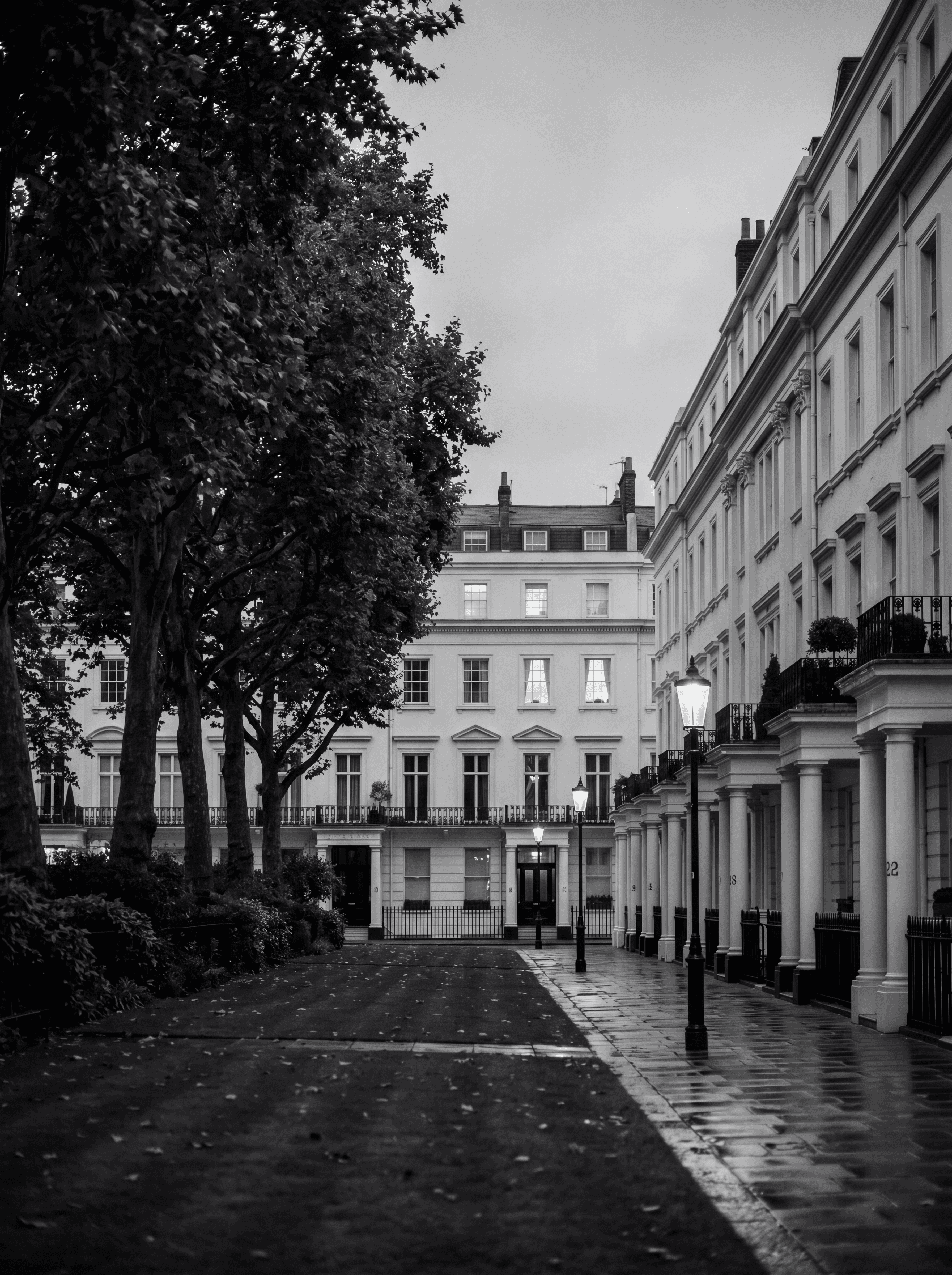 Eaton Square in Belgravia at dusk with white stucco mansions and warm illuminated windows, illustrating concentration of Prime Central London liquidity, monochrome editorial photograph