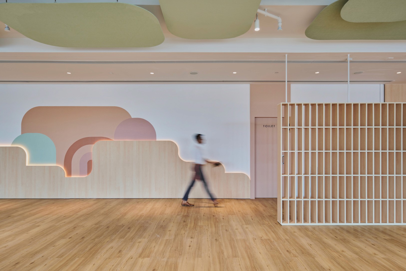 A vibrant activity room characterized by colorful cloud-shaped wall cutouts, light wooden floors, and a decorative slatted partition.