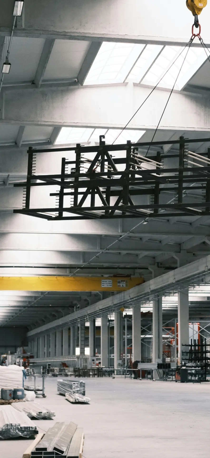 Structural steel truss lifting inside industrial fabrication facility with overhead crane and assembled steel members