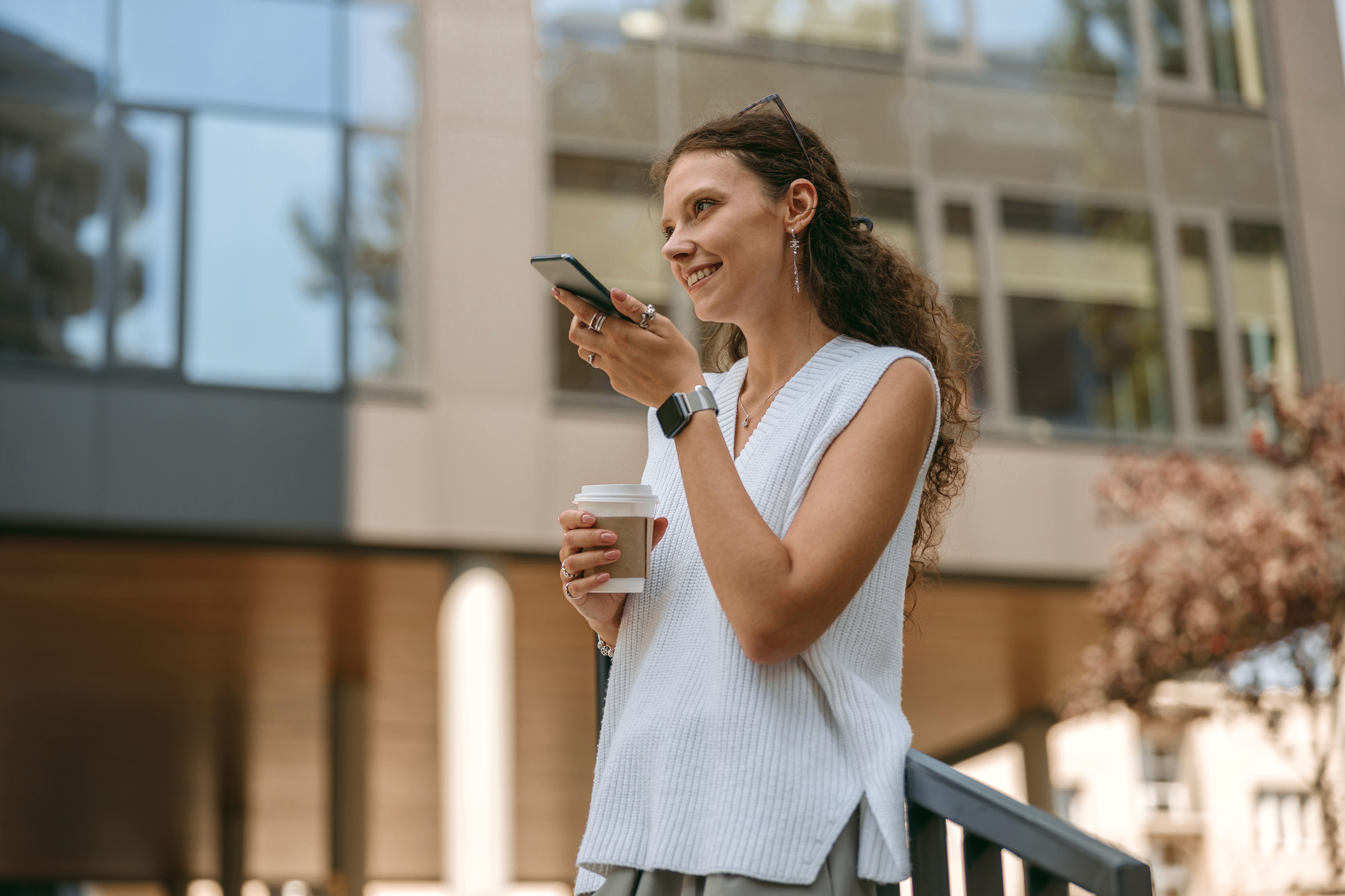 Smiling young woman with long hair standing against a dark green background, holding a finger to her chin.