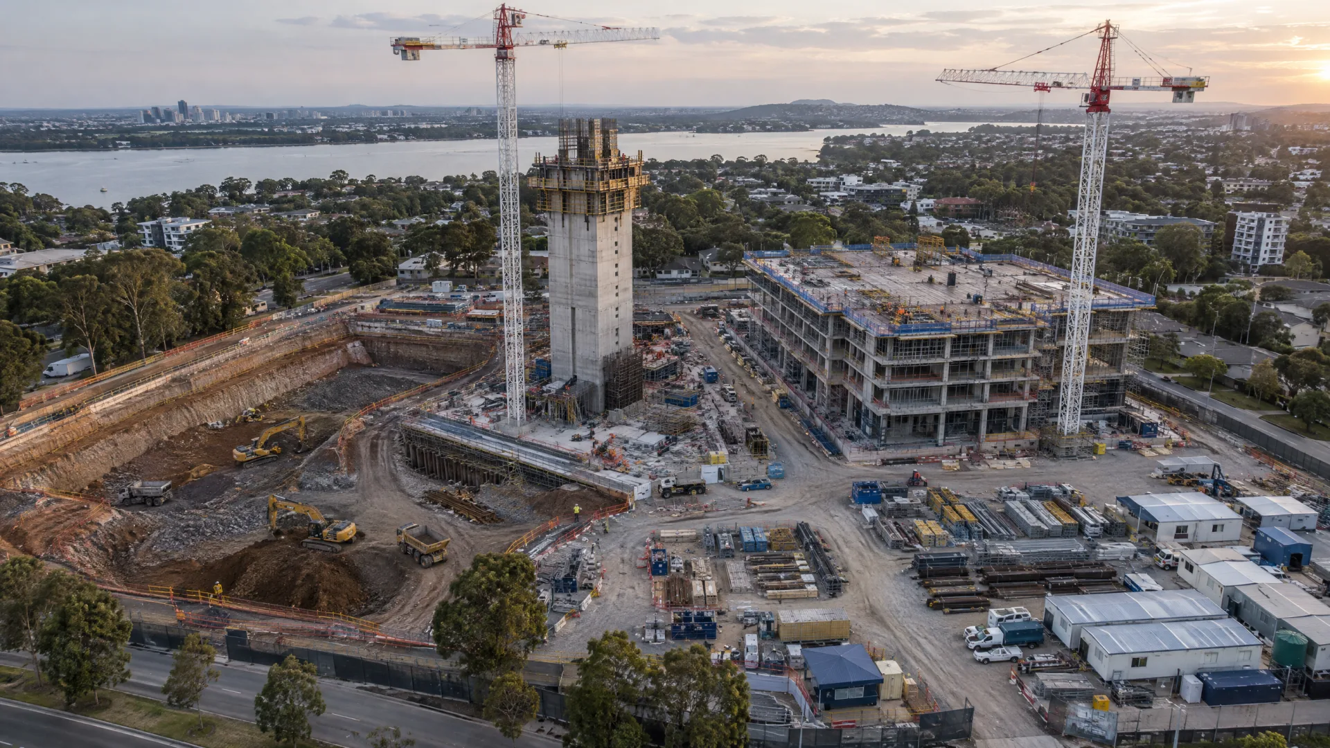 Aerial view of a large construction site with excavation, a rising core and a topped-out building in sequence