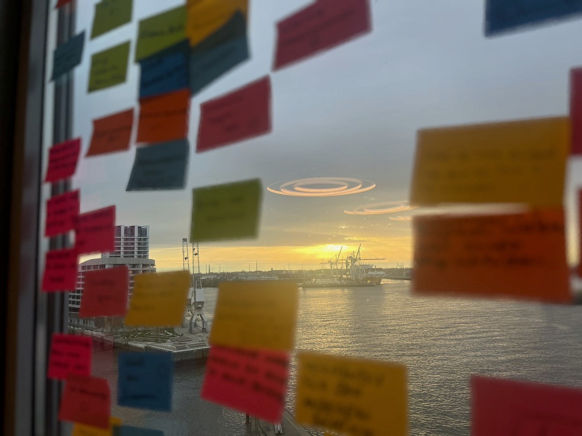 A smiling woman with her arms crossed, standing against a dark green background. She has long, dark hair.