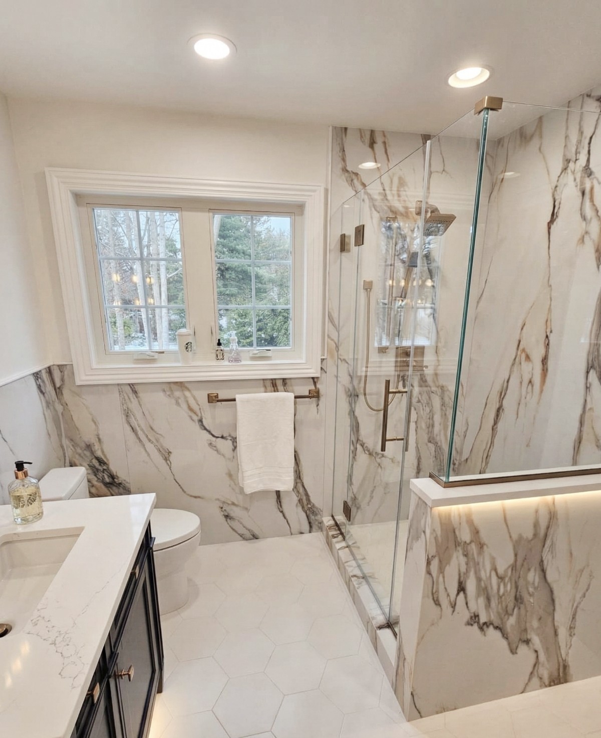 Bathroom renovation with marble tile walls, glass shower enclosure, and modern brass fixtures